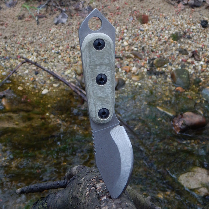 2023 Shed Knives Skur in OD Green sticking out of a branch in a river.